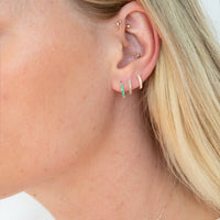 Close-up of a person wearing multiple gold and green hoop earrings - silver birthstone hoops - seolgold