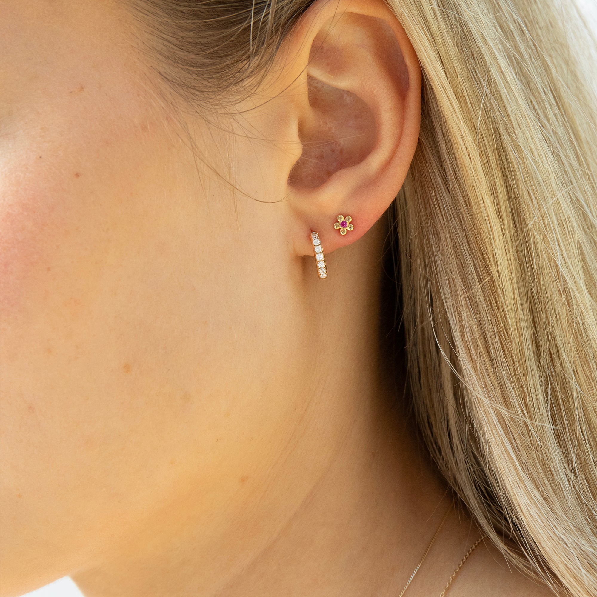Close-up of a person wearing a diamond hoop and floral stud earring with a blurred background - seolgold