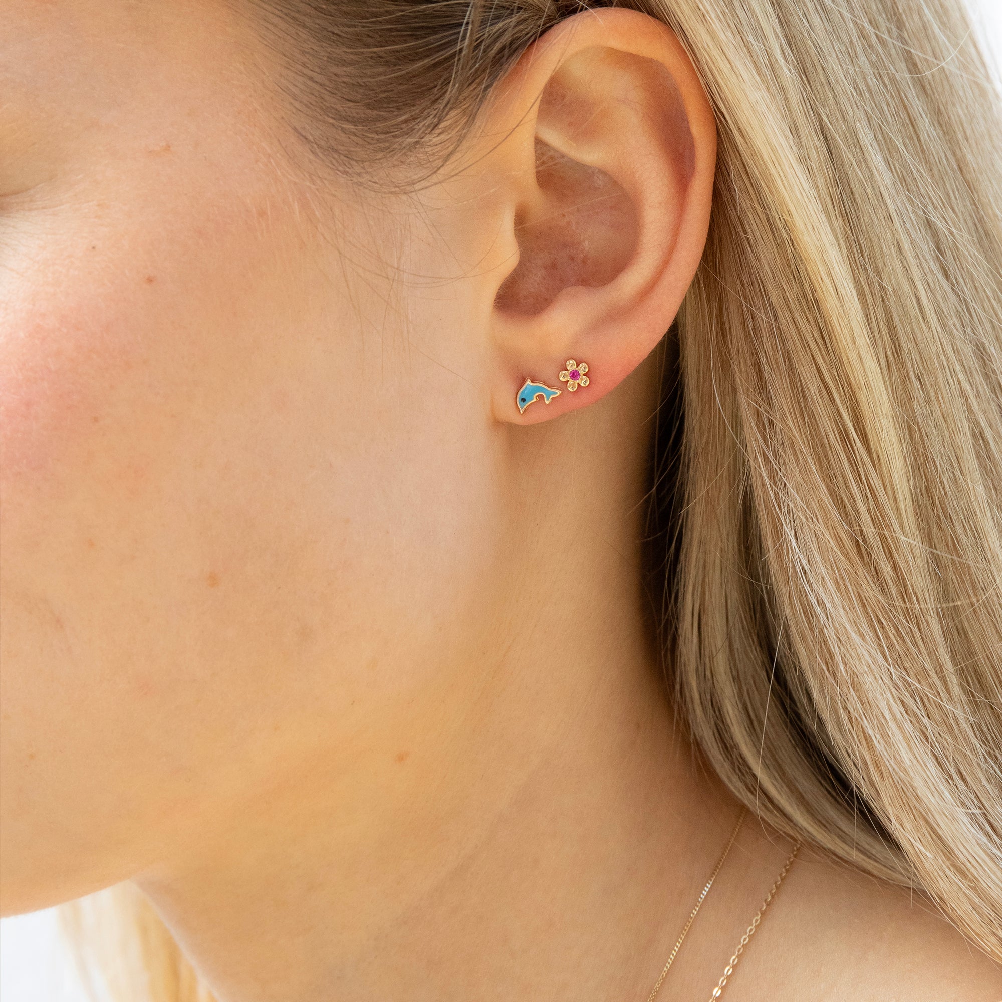 Close-up of an ear wearing a floral earring with a blue dolphin charm - seolgold