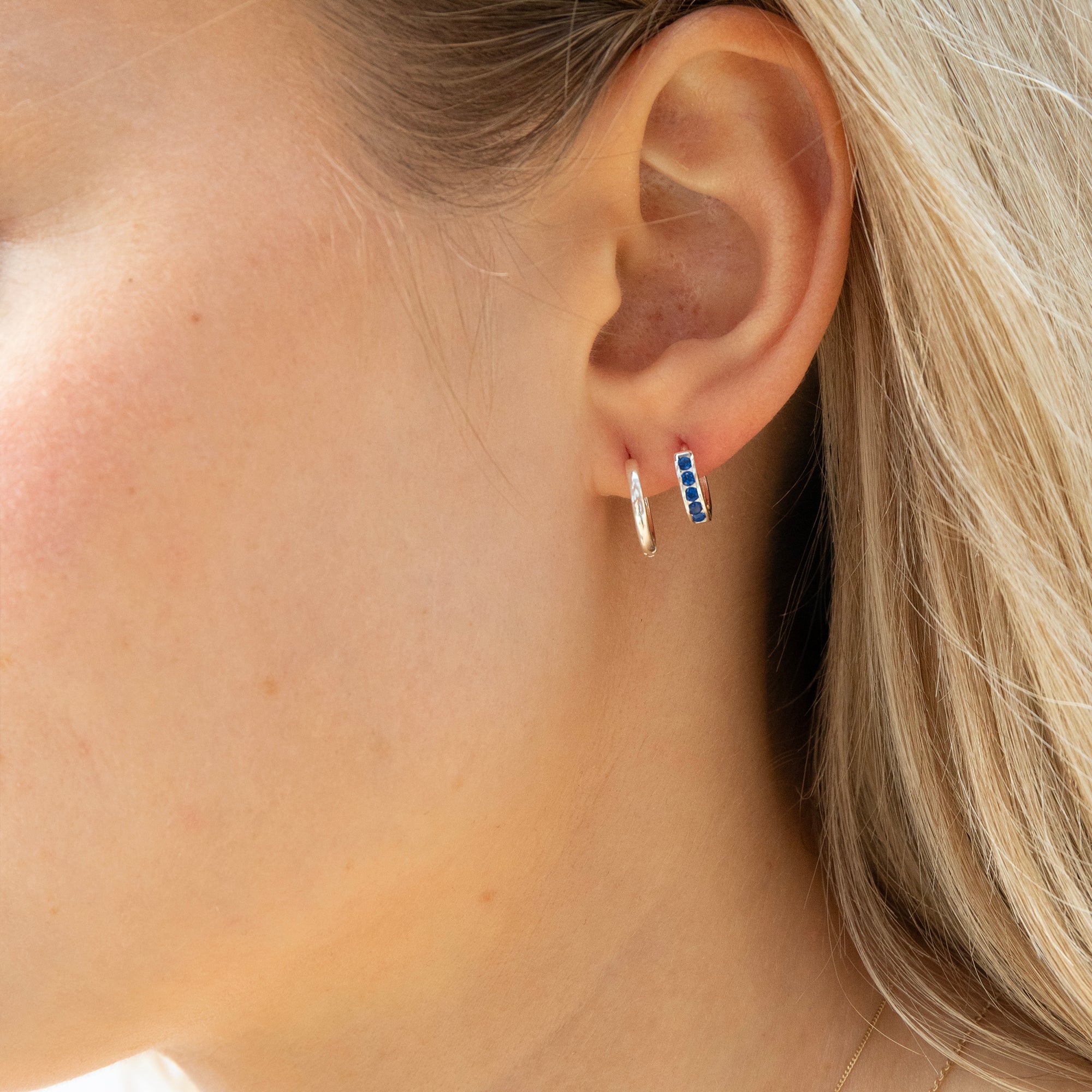 Close-up of an ear wearing a silver hoop earring with blue gemstones - seolgold