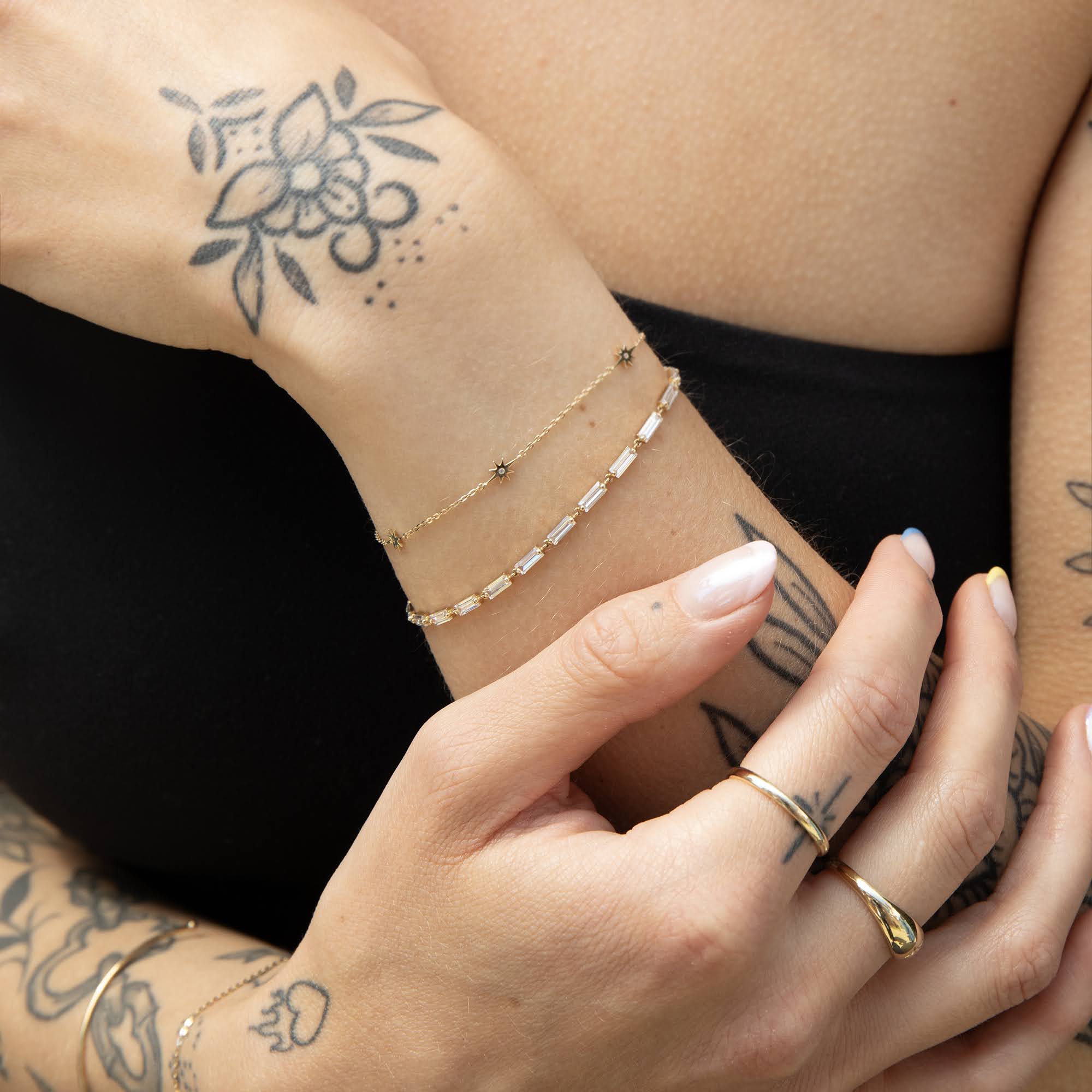 Close-up of a person's arm with gold bracelets and rings, showcasing tattoos and delicate skin - seolgold