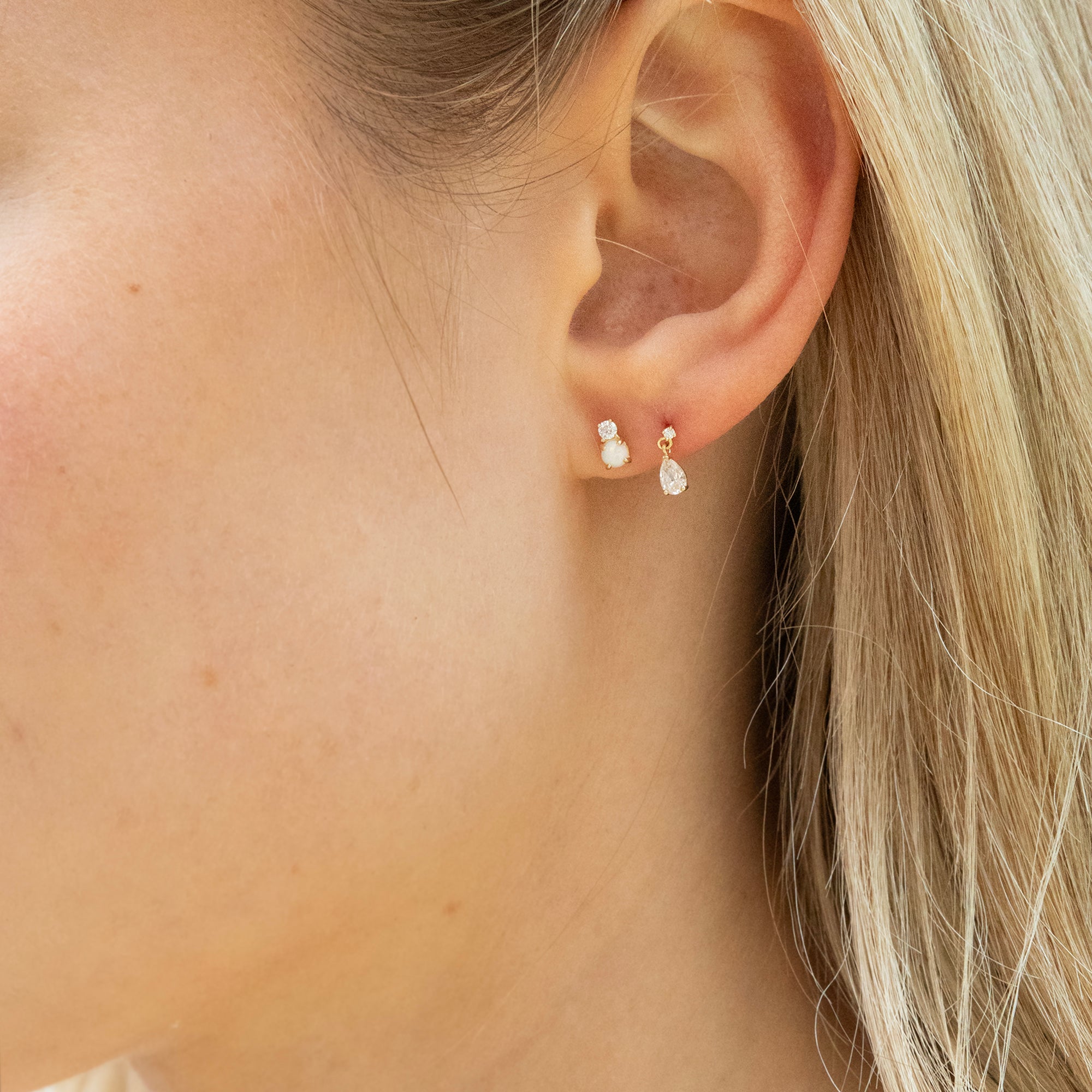 Close-up of an ear wearing a pair of pearl earrings with blonde hair partially visible - seolgold