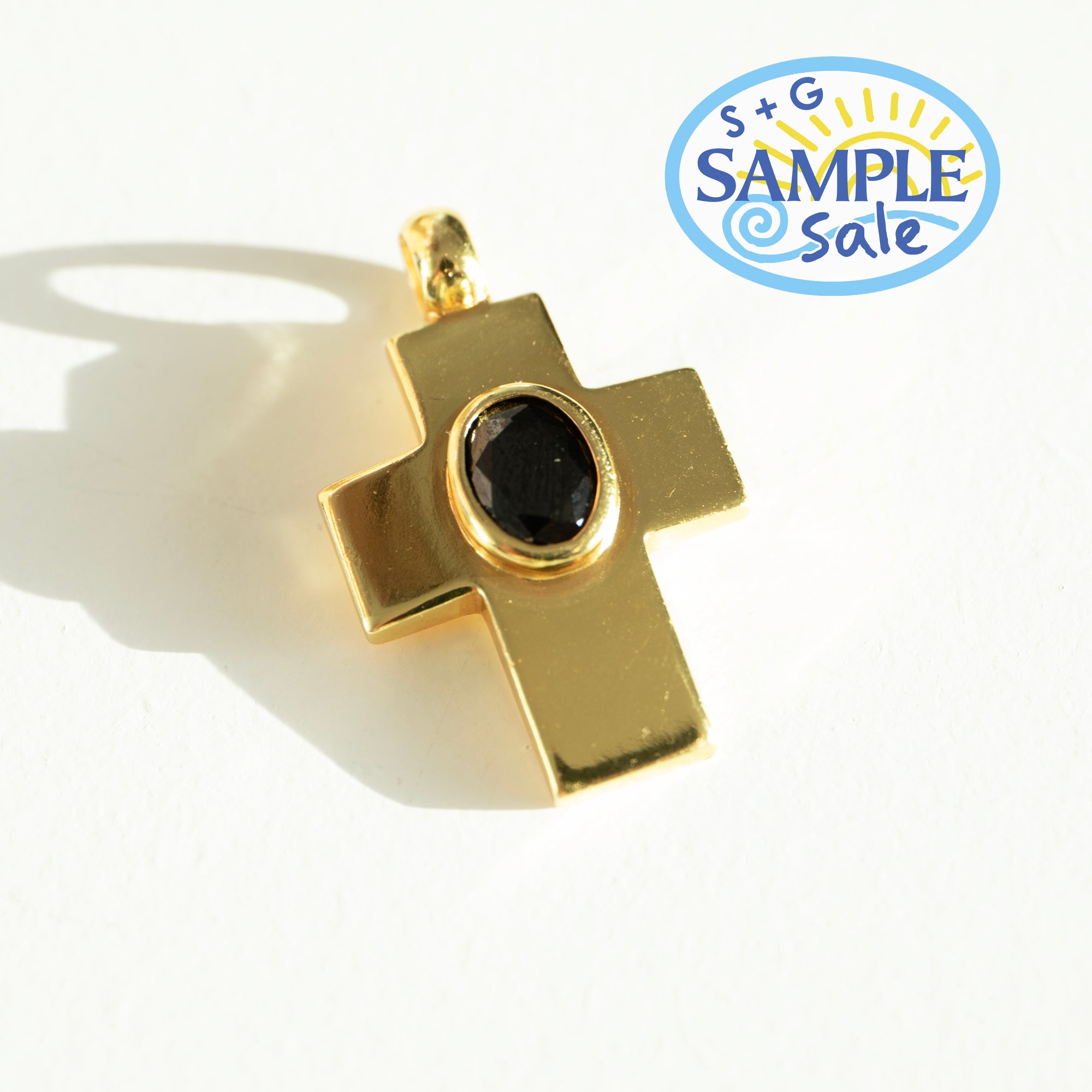 Gold cross pendant with a black gemstone on a white background, featuring a 'Sample Sale' label.