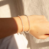 Close-up of a wrist wearing multiple bracelets on a neutral background - seolgold