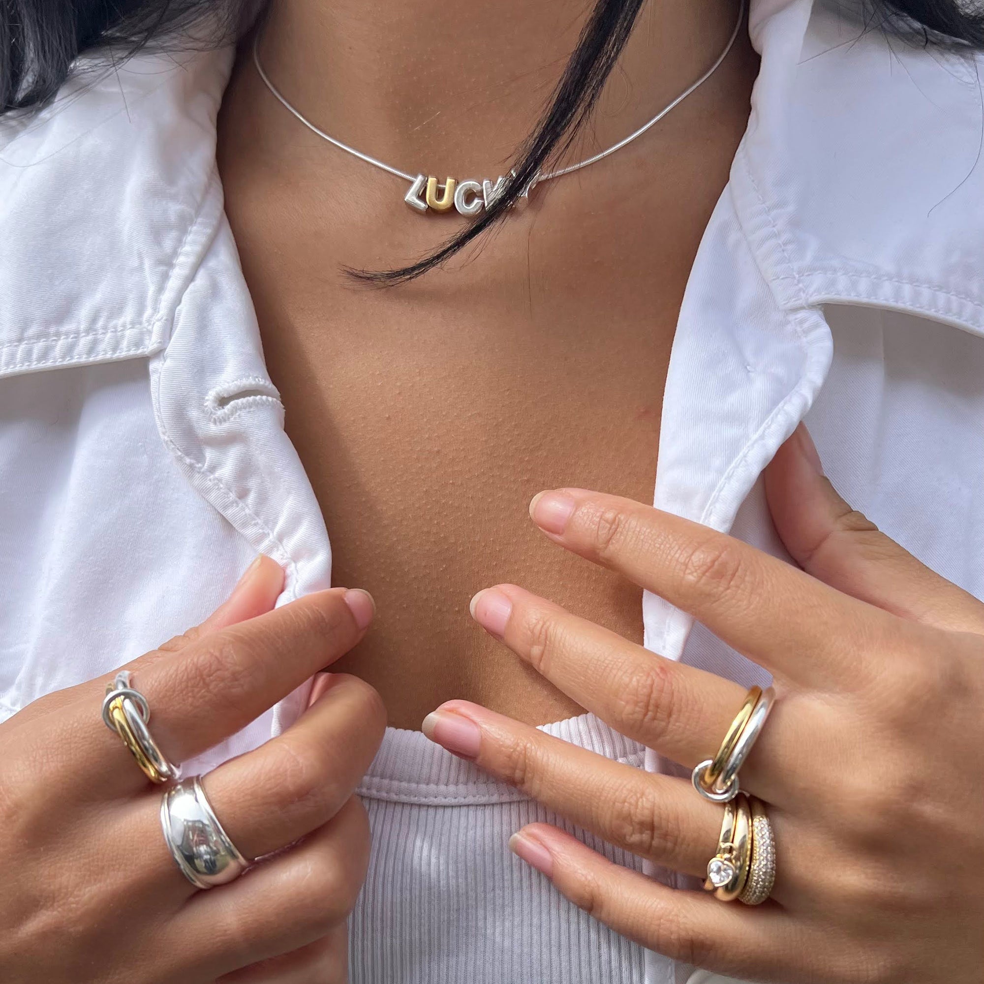 Close-up of a person wearing multiple rings on their fingers with a white jacket and necklace - seolgold