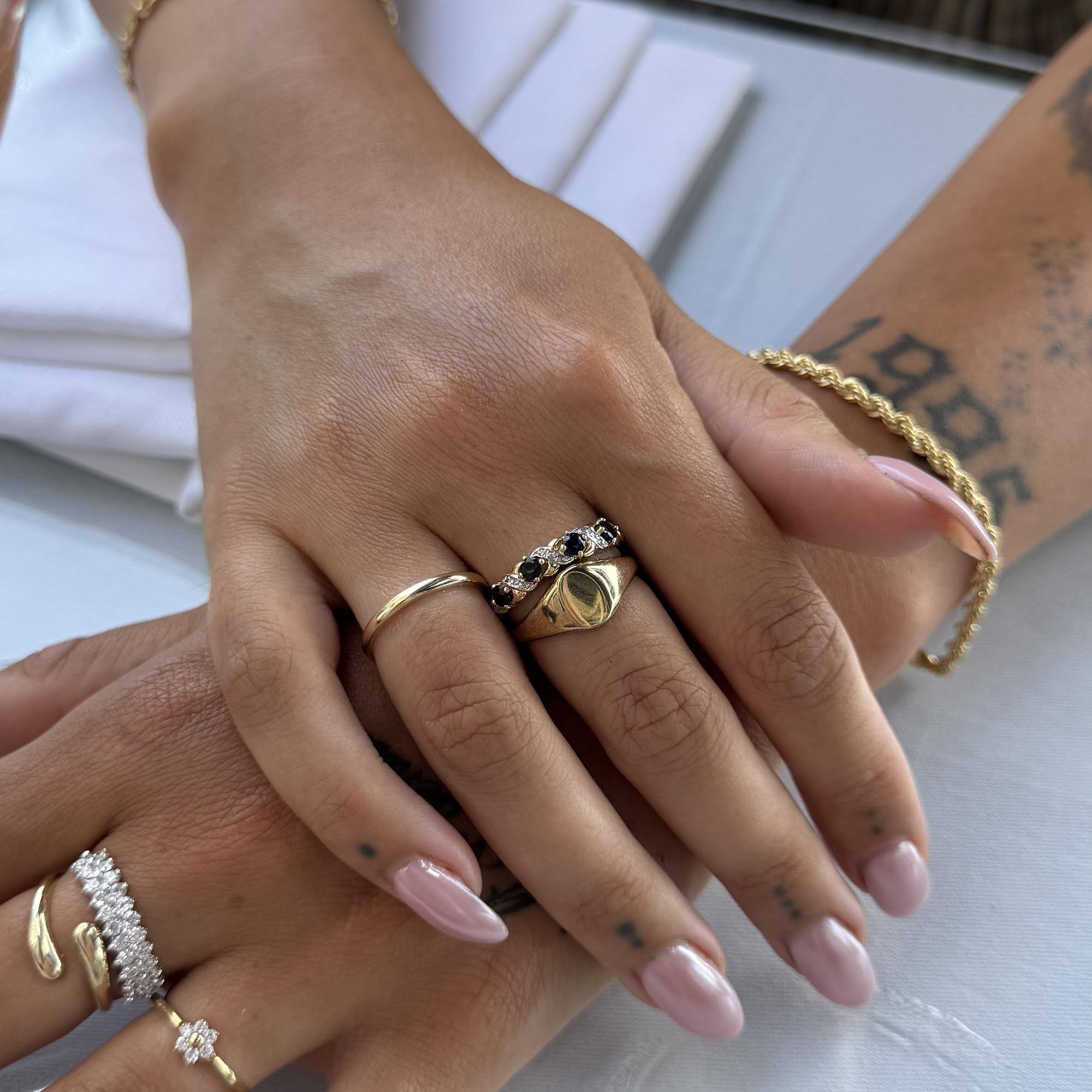 Close-up of hands with multiple gold rings on a light background - seolgold