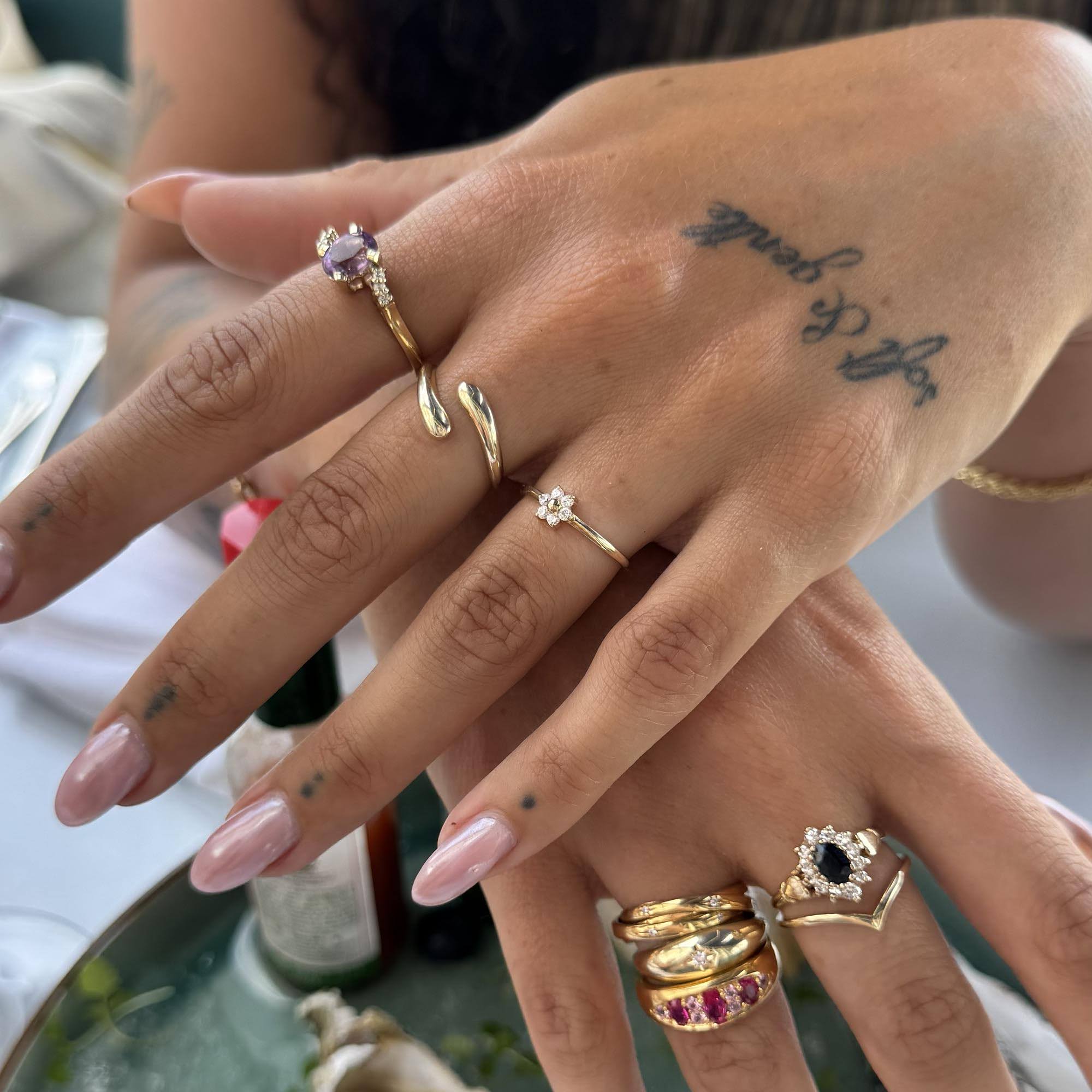 Close-up of a hand wearing multiple gold rings with gemstones on a blurred background - seolgold