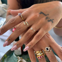 Close-up of a hand wearing multiple gold rings with gemstones on a blurred background - seolgold