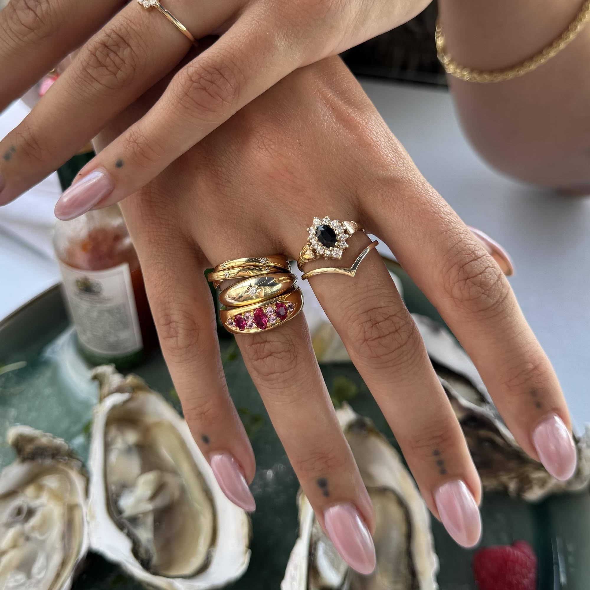 Hand wearing multiple rings with a blurred background of oysters and a bottle. - seolgold