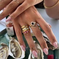 Hand wearing multiple rings with a blurred background of oysters and a bottle. - seolgold
