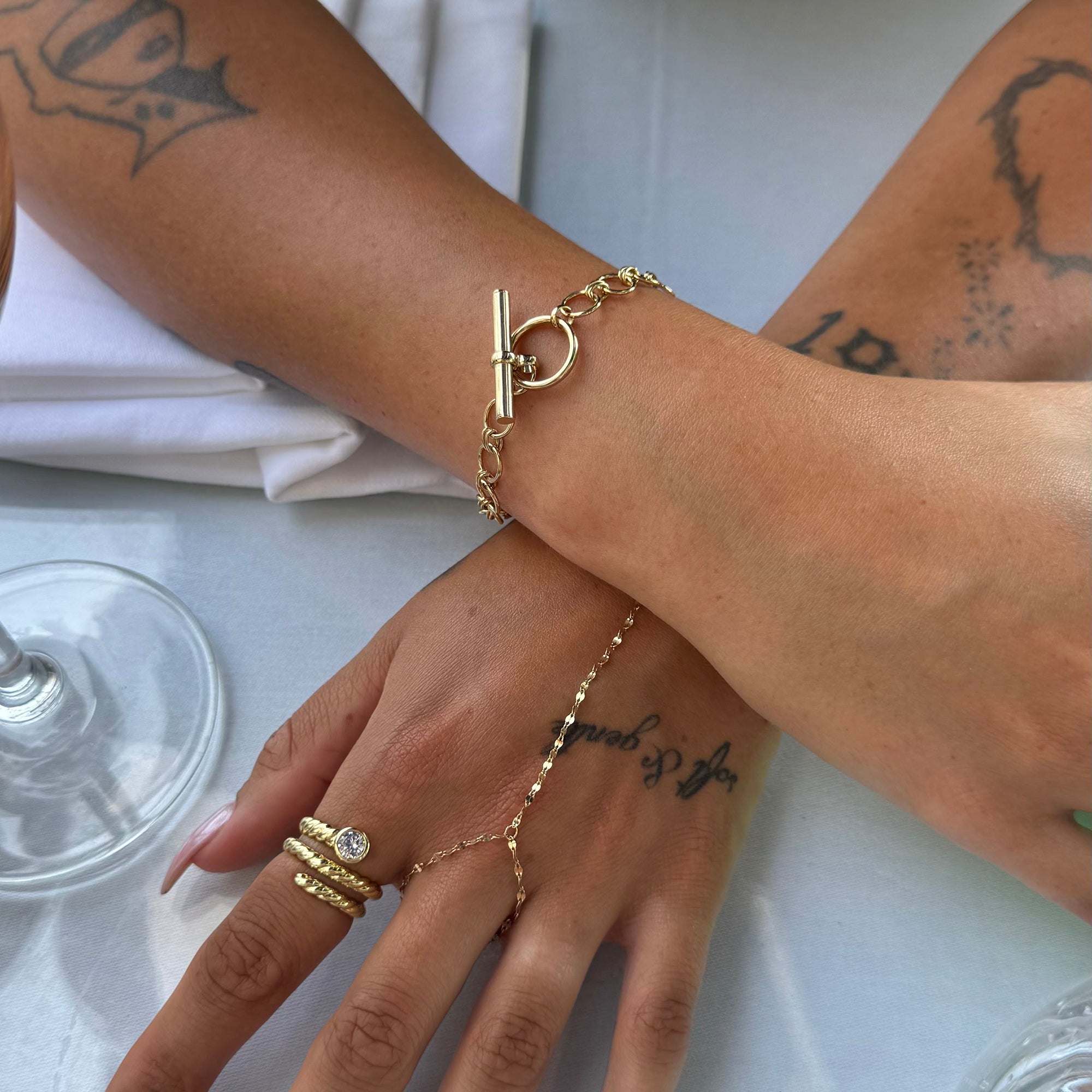 Gold bracelet and ring on a wrist with tattoos, against a white background - seolgold