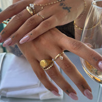 Close-up of a hand with gold rings and pink nail polish holding a glass of white wine - seolgold