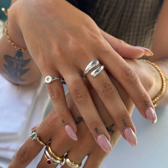 Close-up of hands with multiple rings and pink nail polish on a blurred background - seolgold