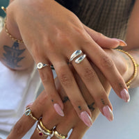 Close-up of hands with multiple rings and pink nail polish on a blurred background - seolgold