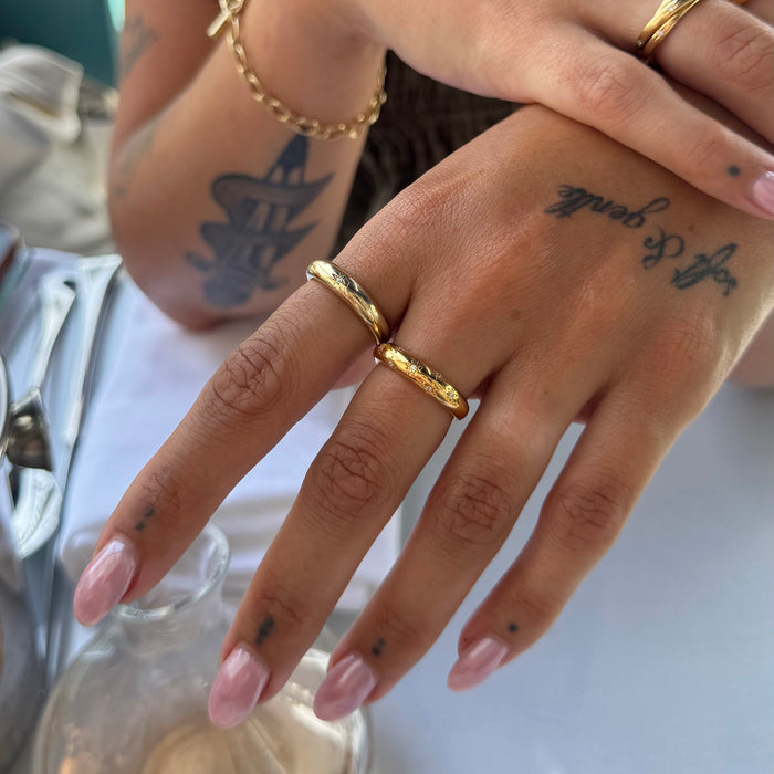 Close-up of a hand with gold rings and tattoos, holding a glass bottle - seolgold