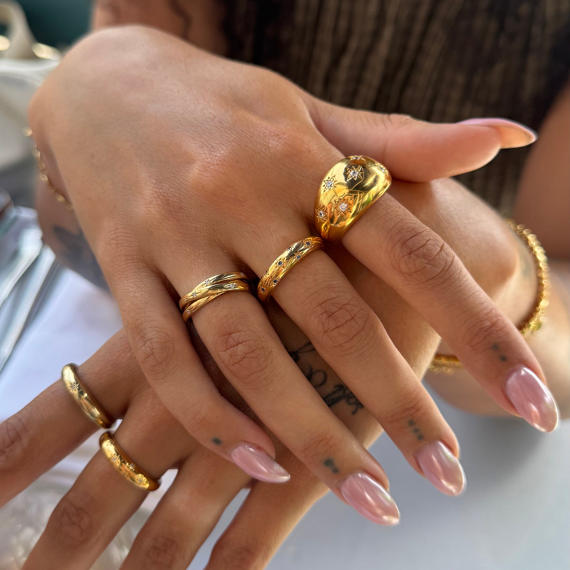 Close-up of a hand wearing multiple gold rings with a blurred background - seolgold