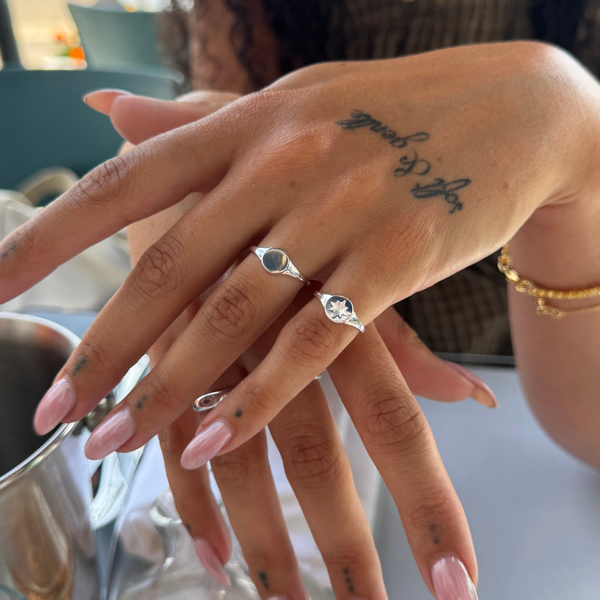Close-up of a hand with multiple silver rings and pink nail polish, with a blurred background - seolgold