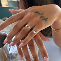 Close-up of a hand with multiple silver rings and pink nail polish, with a blurred background - seolgold