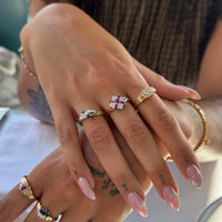 A close-up of a person's hands wearing multiple gold rings with different gemstone designs, including a prominent ring with a pink and white crystal cluster - seolgold