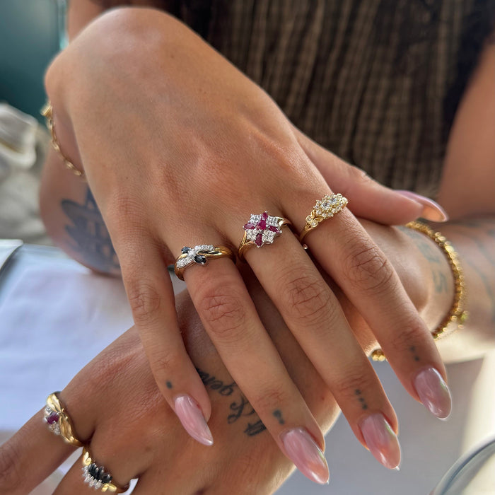 A close-up of a person's hands wearing multiple gold rings with different gemstone designs, including a prominent ring with a pink and white crystal cluster - seolgold