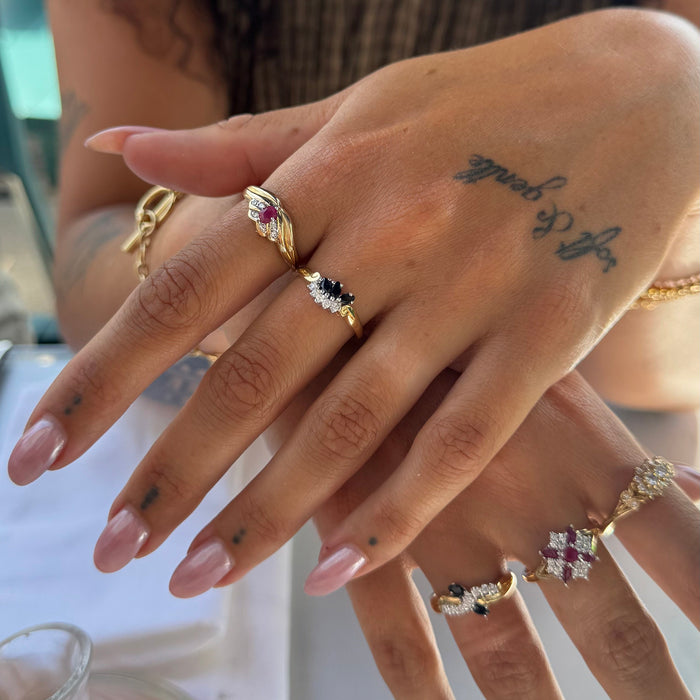 A close-up of a person's hands wearing multiple gold rings with colorful gemstones, including pink, black, and white stones - seolgold