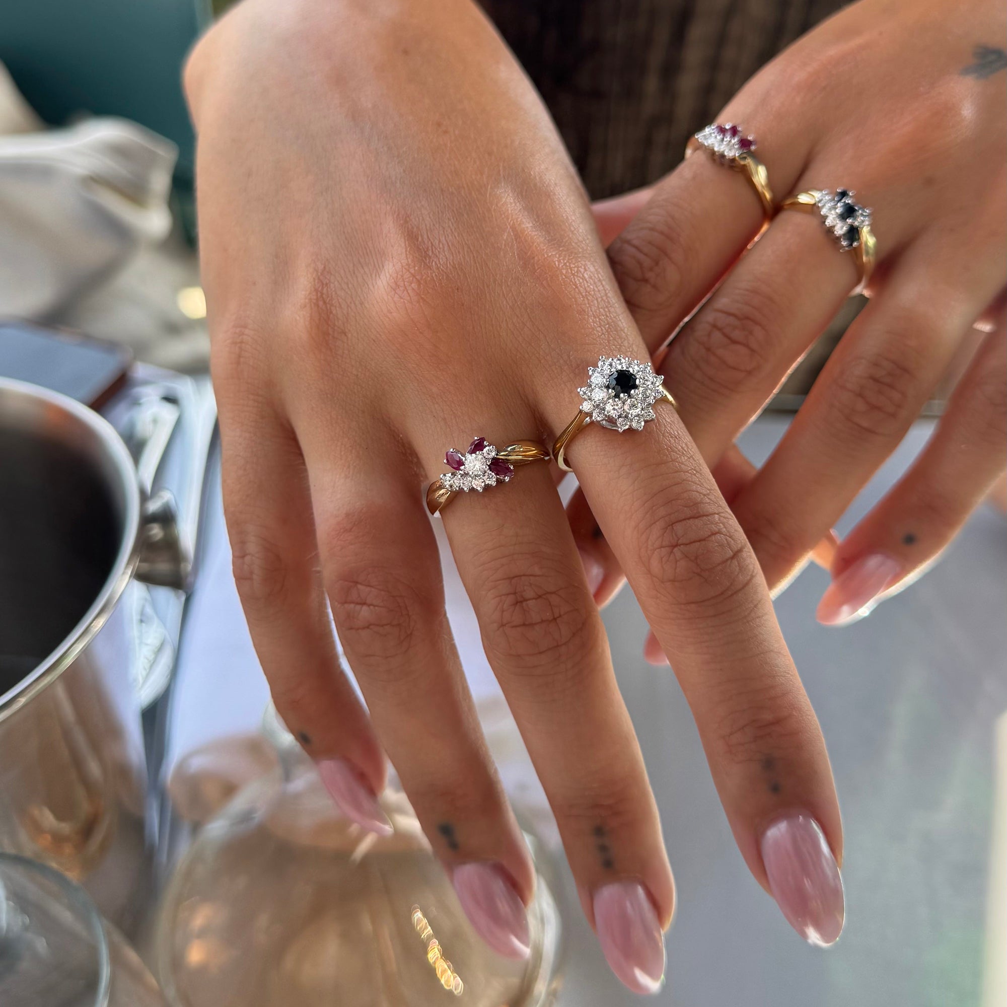 Close-up of a hand wearing multiple rings with gemstones, with a blurred background - seolgold