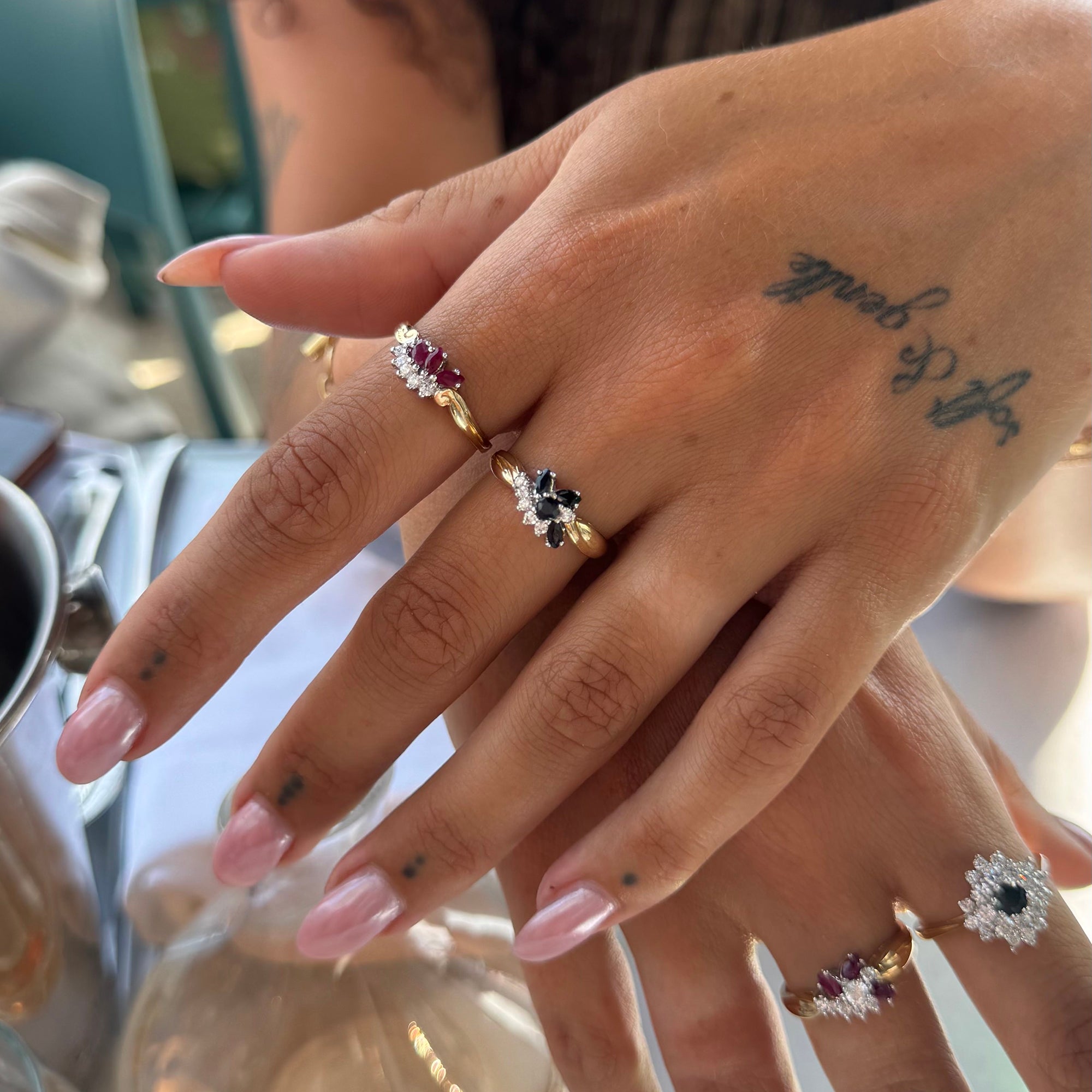 Close-up of a hand wearing two gold rings with gemstones, with a blurred background - seolgold