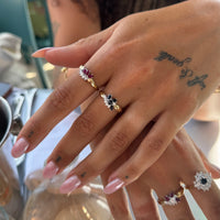 Close-up of a hand wearing two gold rings with gemstones, with a blurred background - seolgold