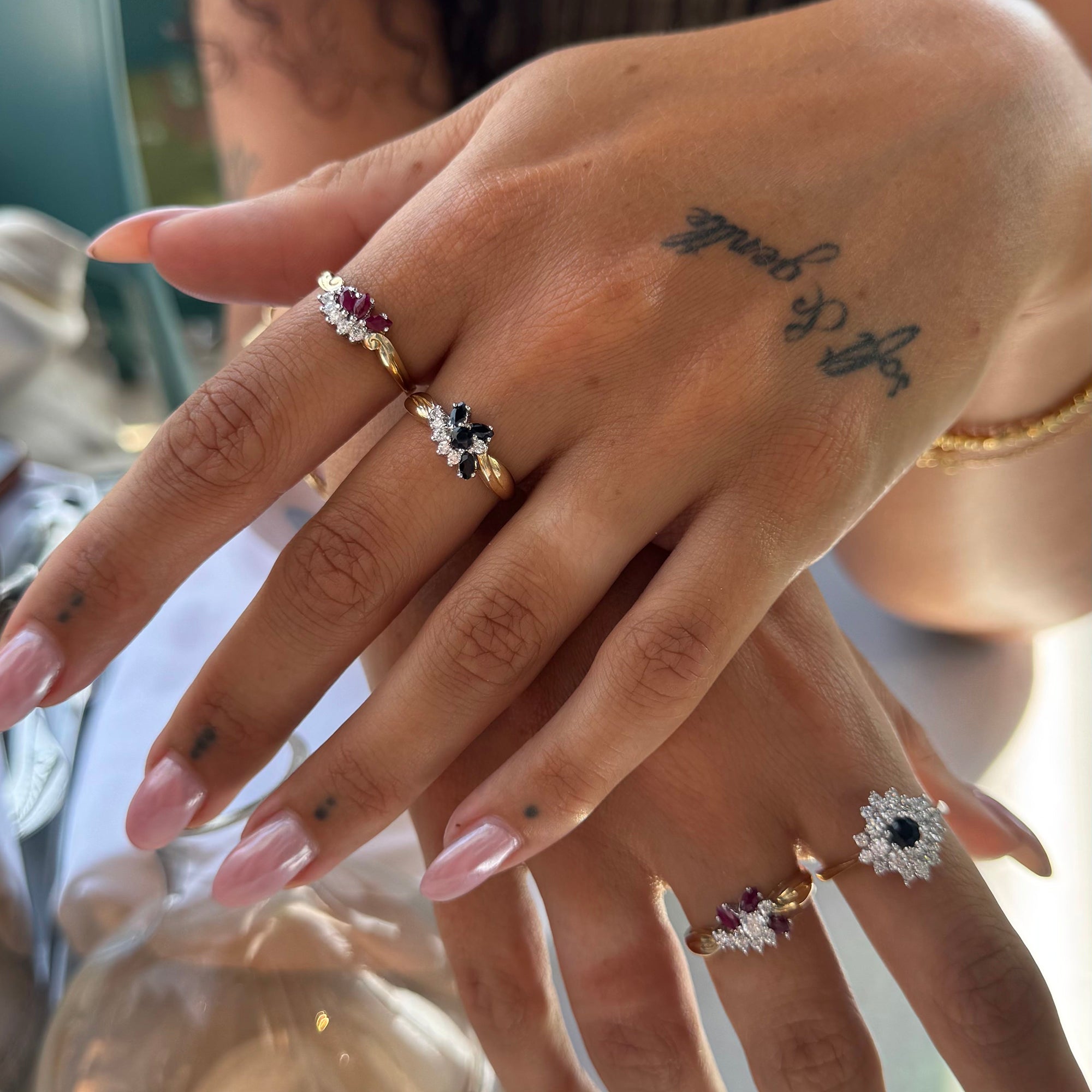 Close-up of a hand wearing multiple rings with gemstones, set against a blurred background - Seolgold