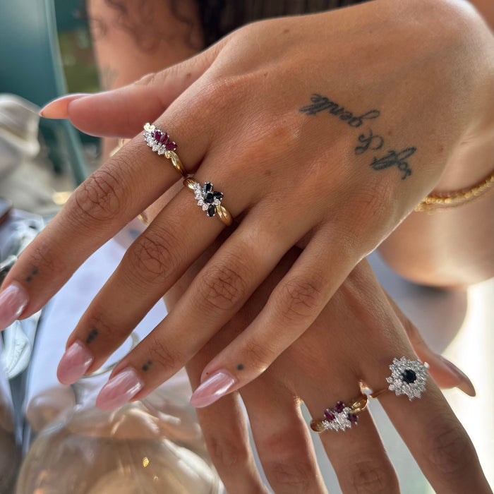 Close-up of a hand wearing multiple rings with gemstones, set against a blurred background - Seolgold