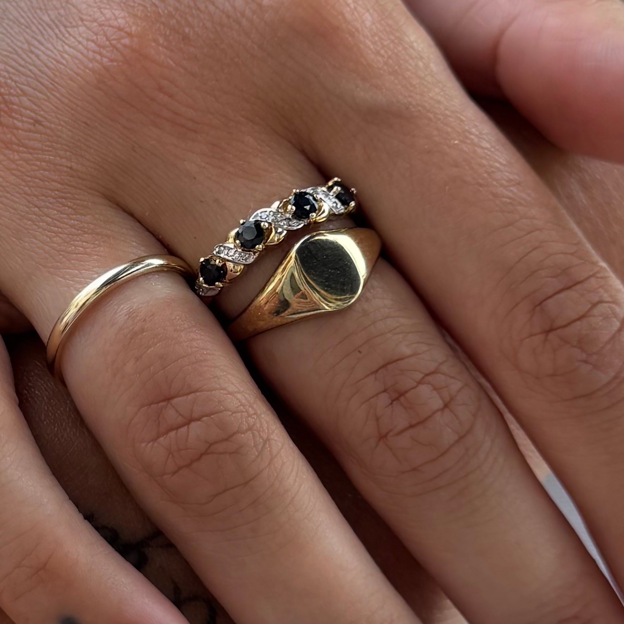 Close-up of fingers wearing gold rings with gemstones on a neutral background - seolgold