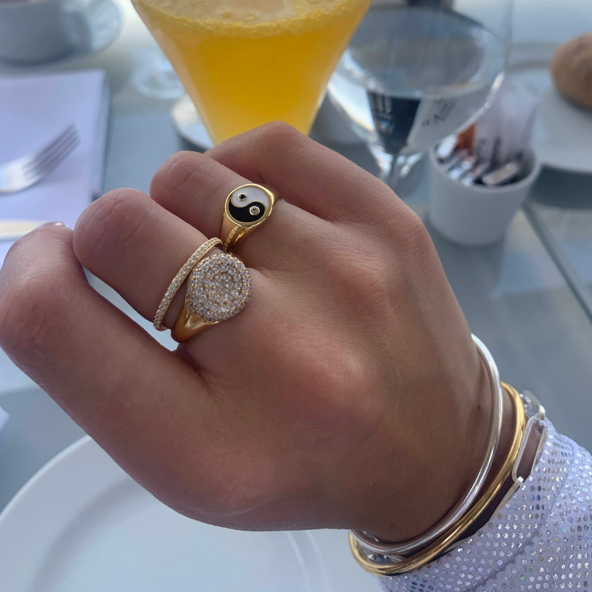 Hand wearing multiple gold rings with a blurred background of a cafe setting - seolgold