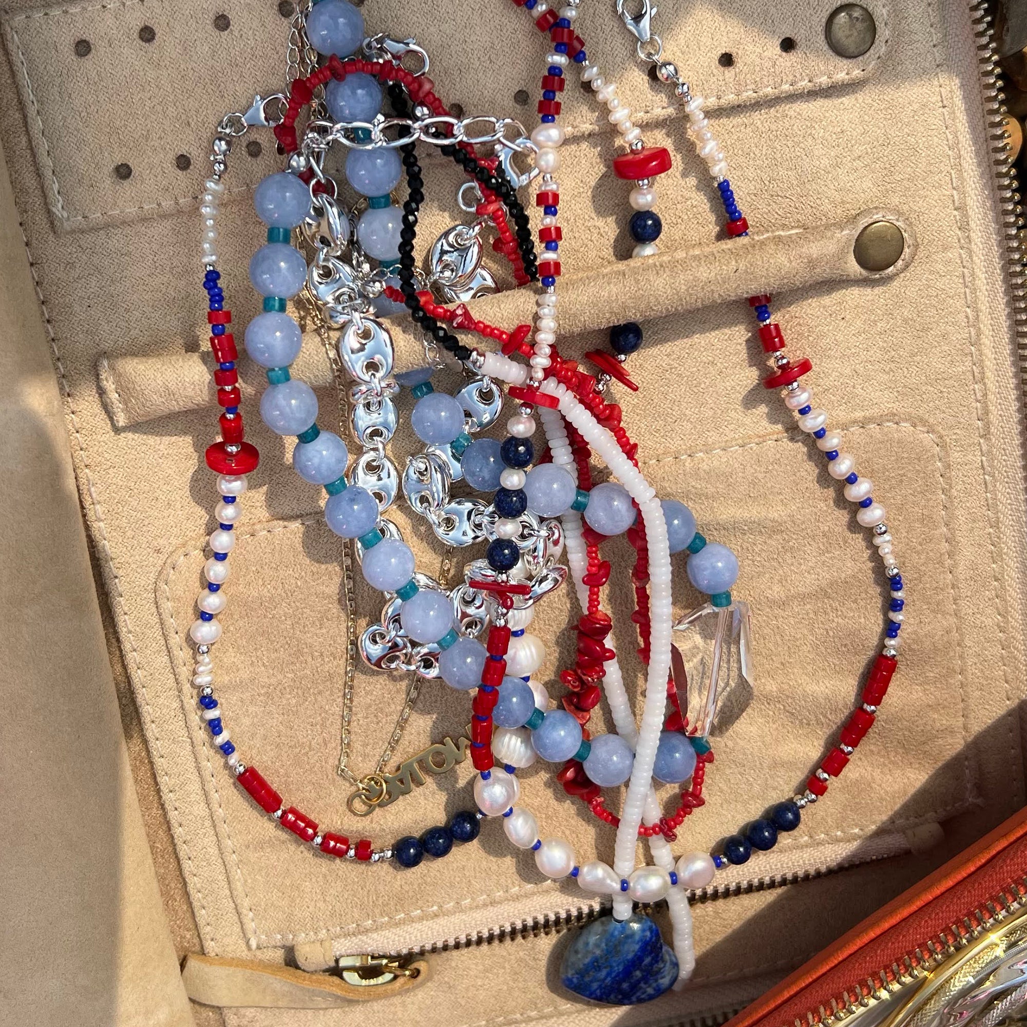 Beaded necklaces with red, blue, and white colors on a beige textured surface - seolgold