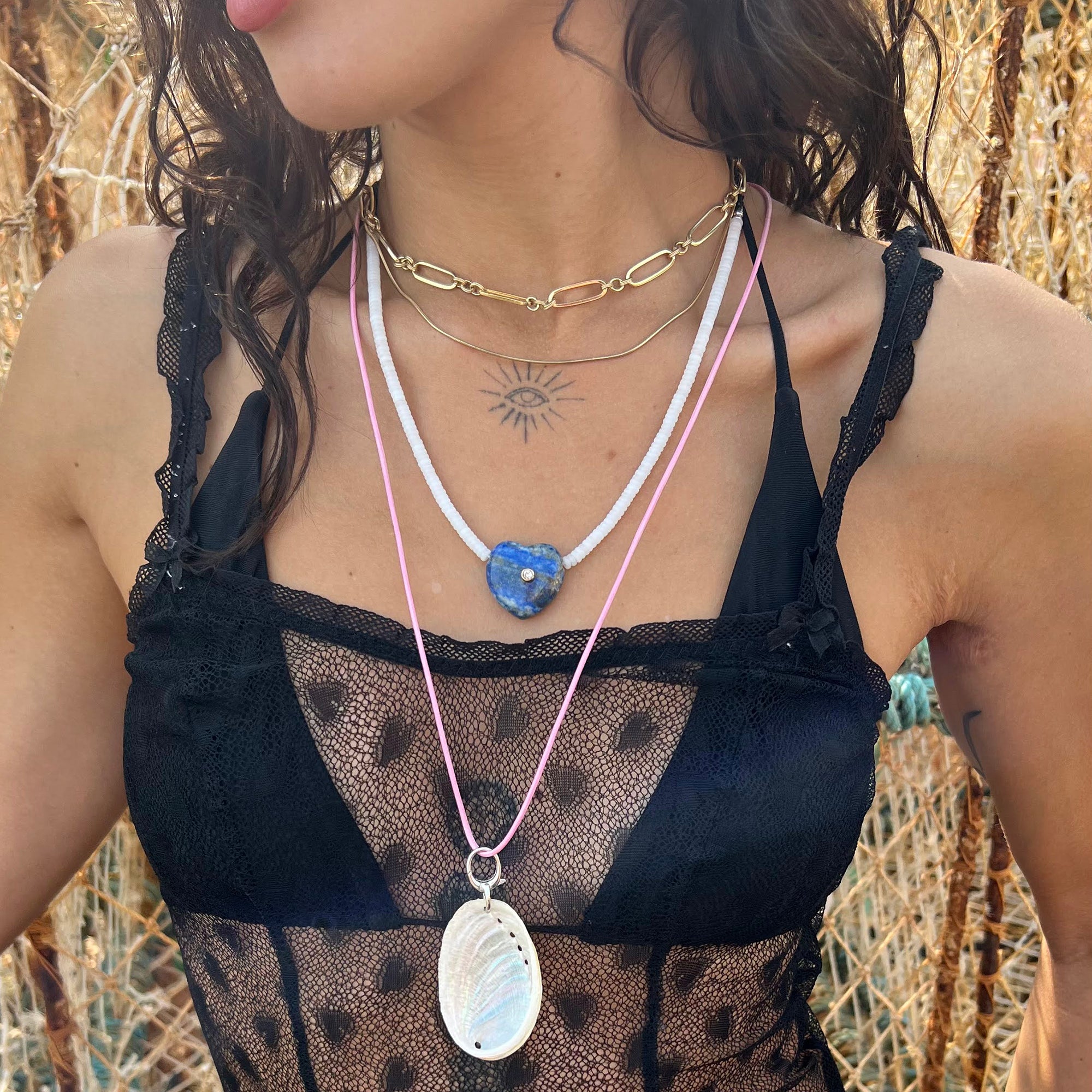 Person wearing multiple necklaces with pendants against a natural background - seolgold