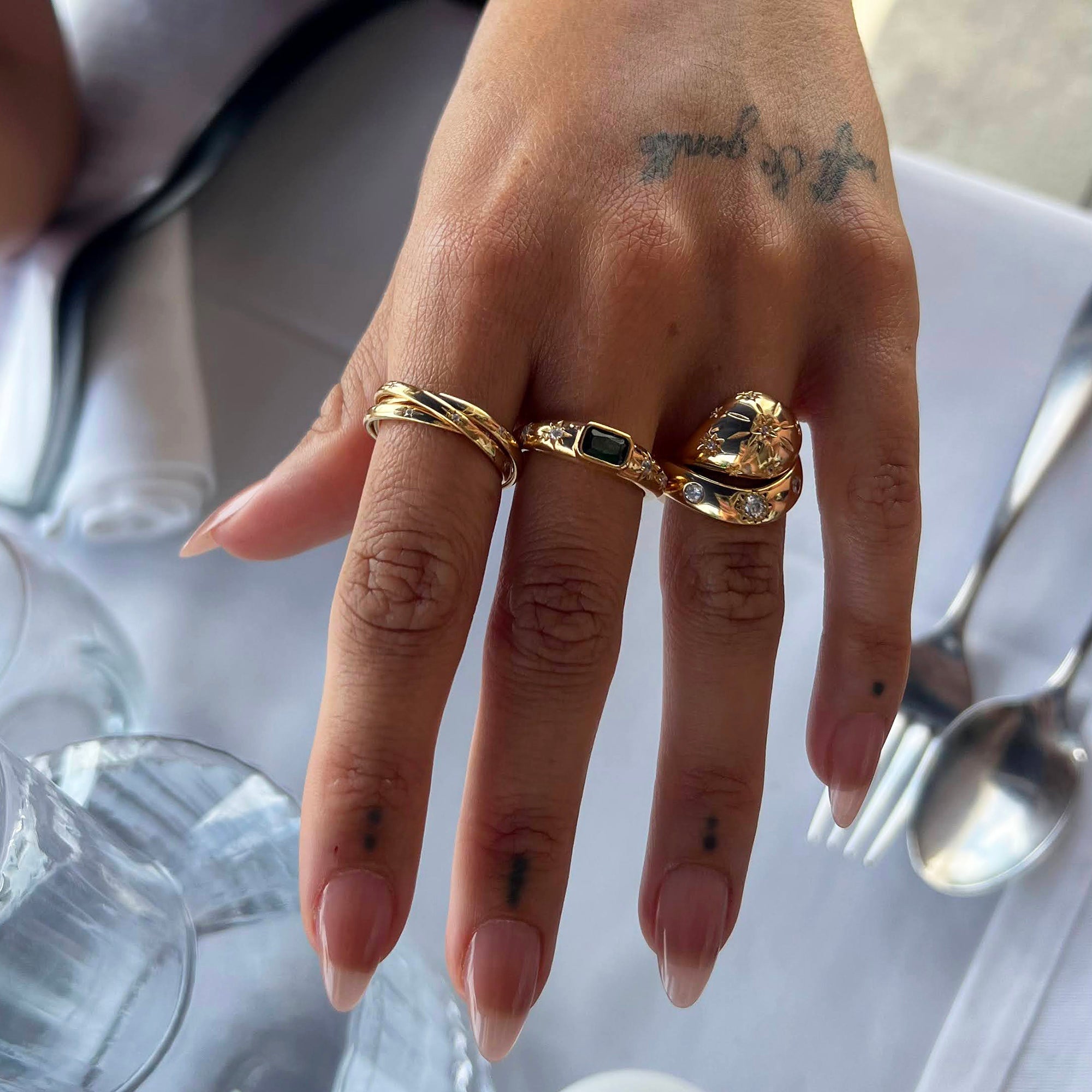 Hand wearing gold rings with tattoos on a white surface - seolgold