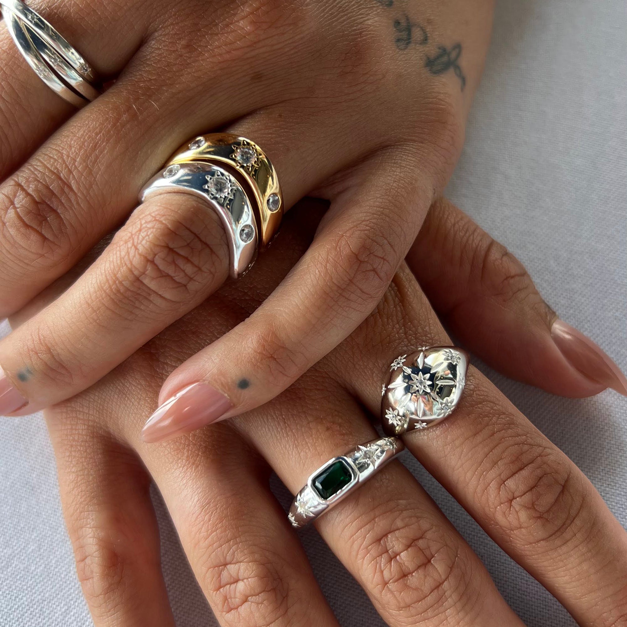 Close-up of a hand wearing multiple rings with gemstones on a light background - seolgold