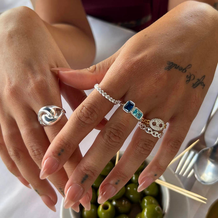 Close-up of hands with multiple silver rings on a blurred background - seolgold