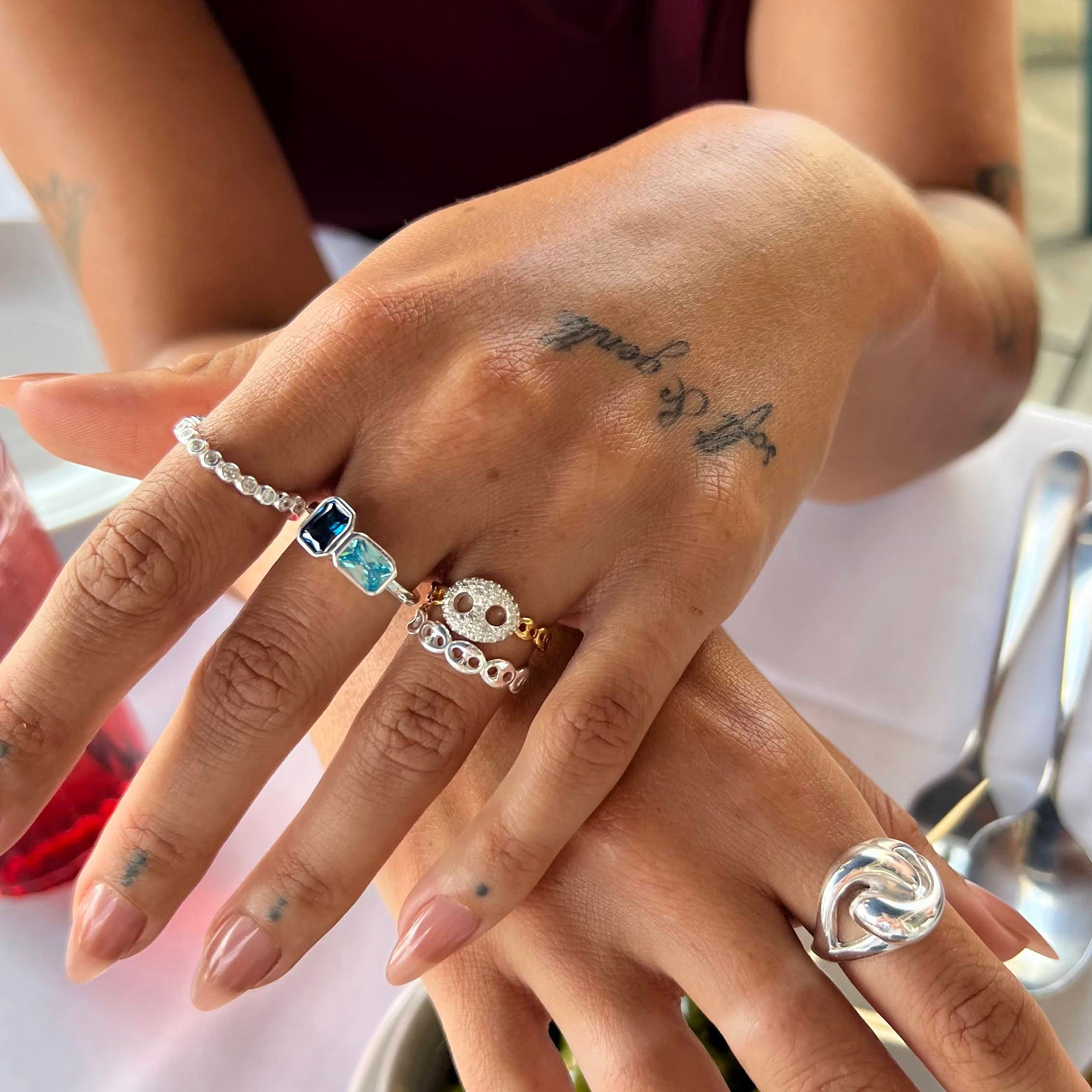 Close-up of a hand with multiple rings and a tattoo, set against a blurred background - seolgold