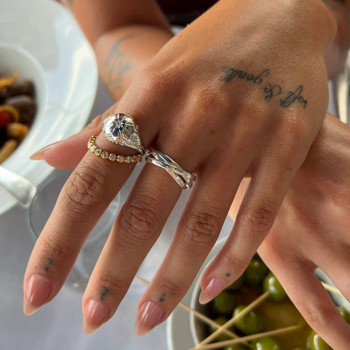 Close-up of a hand with multiple rings and tattoos, with a blurred background - seolgold