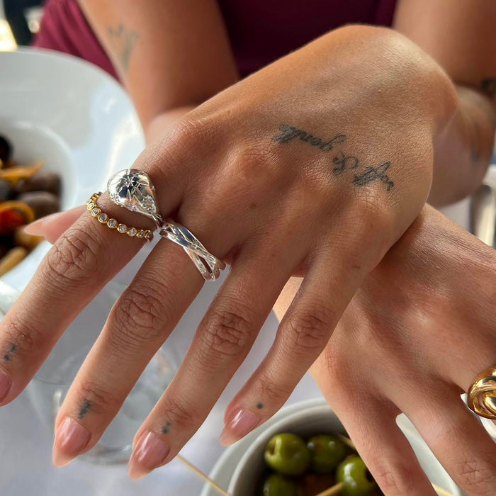 Close-up of a hand with multiple rings and tattoos, set against a blurred background - seolgold