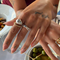 Close-up of a hand with multiple rings and tattoos, set against a blurred background - seolgold