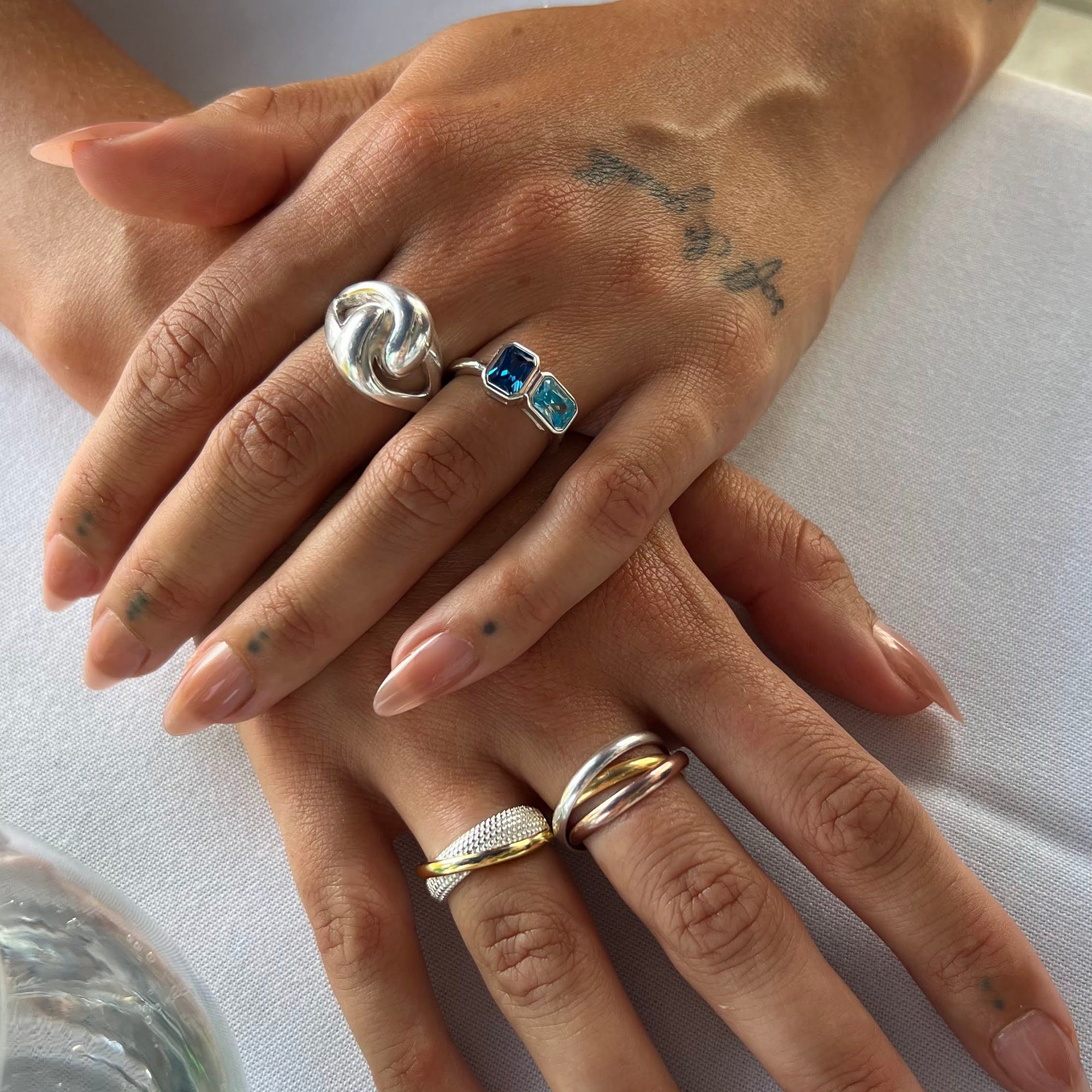 Close-up of hands wearing multiple rings on a light background - seolgold