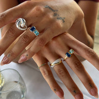 Close-up of hands wearing multiple  silver and gold rings with gemstones on a blurred background - seolgold