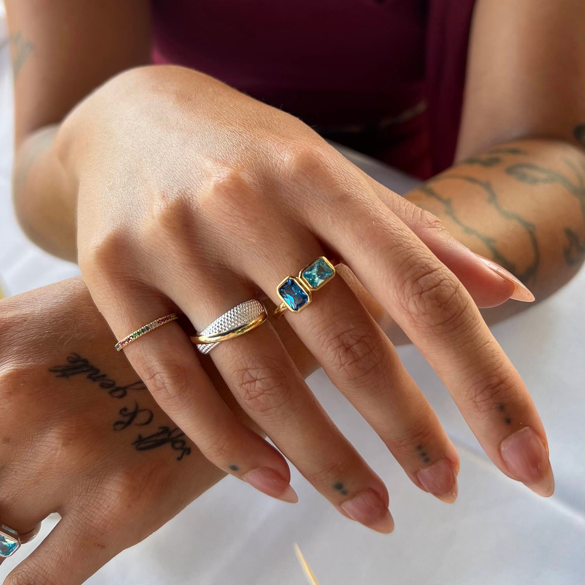 Close-up of hands wearing multiple rings with a tattoo on the arm - seolgold