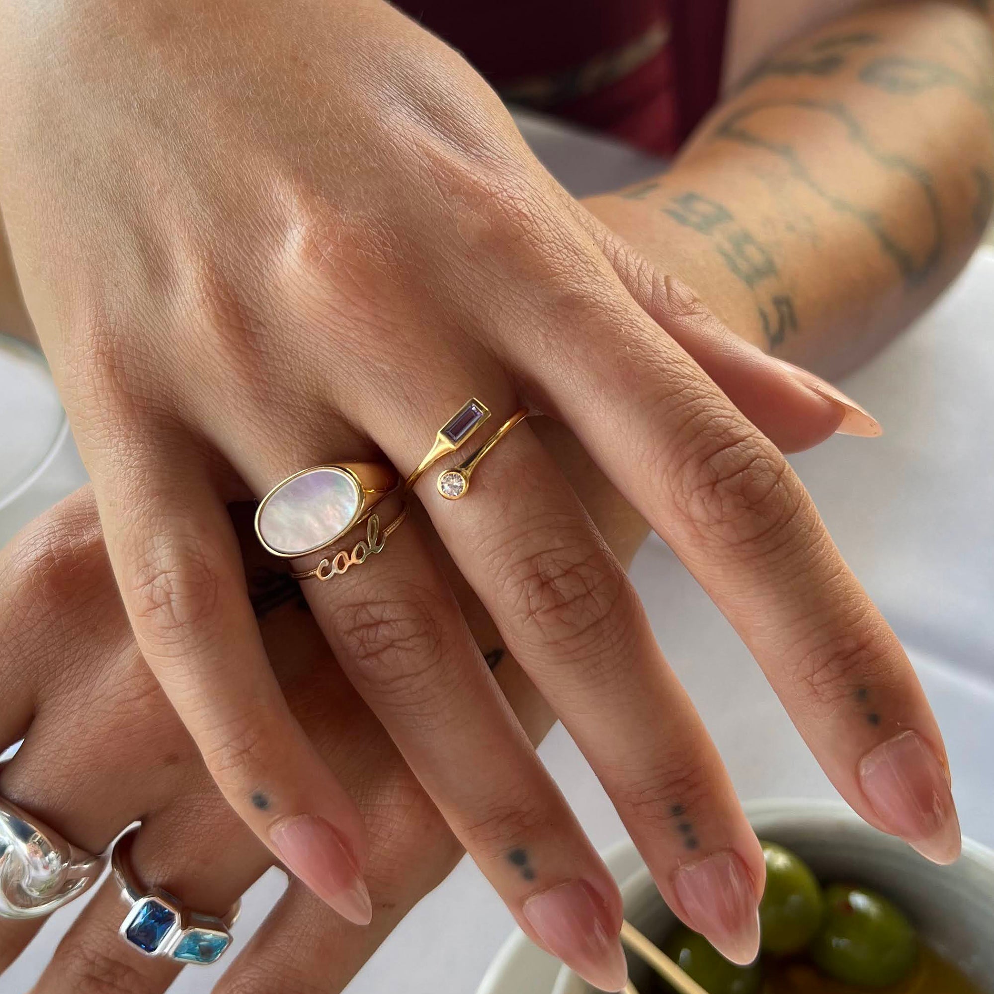 Close-up of hands with multiple rings on a neutral background - solid gold 'cool' ring - seolgold