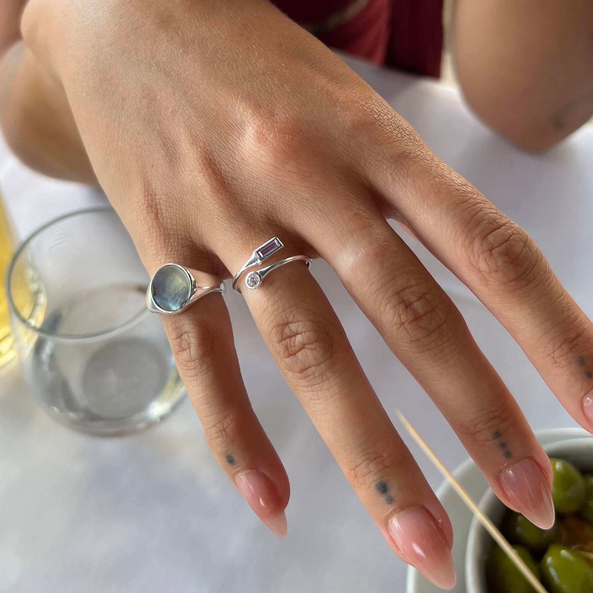 Close-up of a hand wearing a silver ring with a gemstone, set against a blurred background - seolgold
