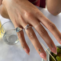 Close-up of a hand wearing a silver ring with a gemstone, set against a blurred background - seolgold