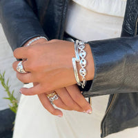 Close-up of a hand wearing multiple silver bracelets and rings against a neutral background - seolgold