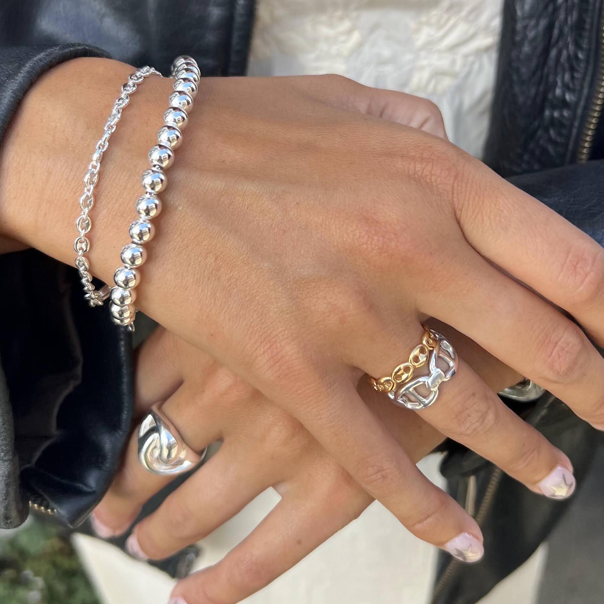 Close-up of a hand wearing silver bracelets and rings with a blurred background - seol gold