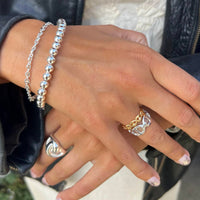 Close-up of a hand wearing silver bracelets and rings with a blurred background - seol gold